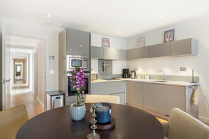 Una cuina moderna amb electrodomèstics integrats, una zona de menjador amb taula rodona i un passadís que condueix a una altra habitació.