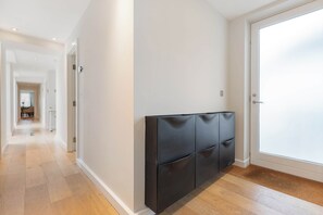Passadís amb un capçal de llit negre i modern al davant d'una paret blanca, que condueix a una porta amb vidre mat.