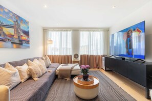 Ein modernes Wohnzimmer mit einer Couch, einem Couchtisch, einem Fernseher und einem Gemälde einer Brücke.