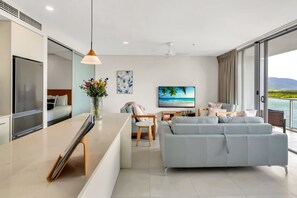 A modern living room with a sofa, a TV, and a dining area. - Belle Escapes 1104 Harbour Lights Top Floor Ocean & City Views (Cairns City)