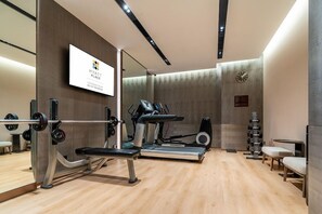 A modern gym with exercise equipment, a mirrored wall, and a clock.