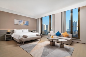 Ein modernes Hotelzimmer mit einem großen Bett, einer Couch, einem Couchtisch und Blick auf die Stadt.
