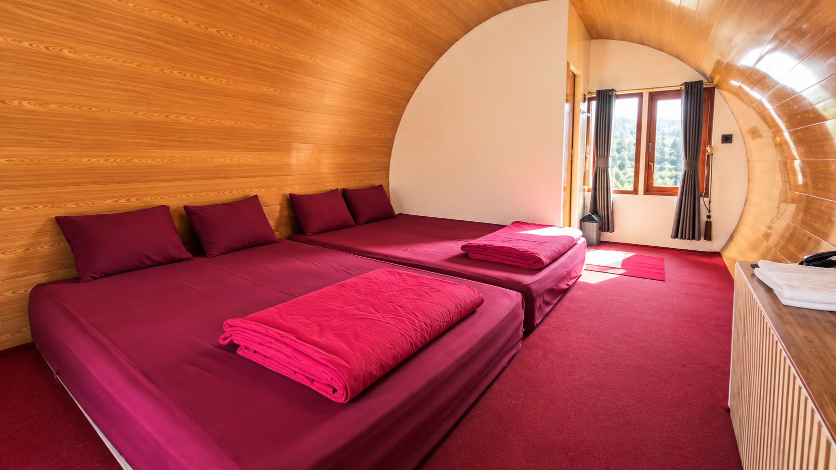 A room with two beds, a wooden ceiling, and a view through a window.