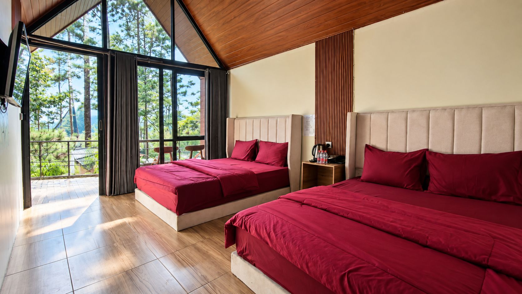 A bedroom with two beds, a wooden floor, and a large window with a view of trees.