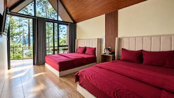 A bedroom with two beds, a wooden floor, and a large window with a view of trees.