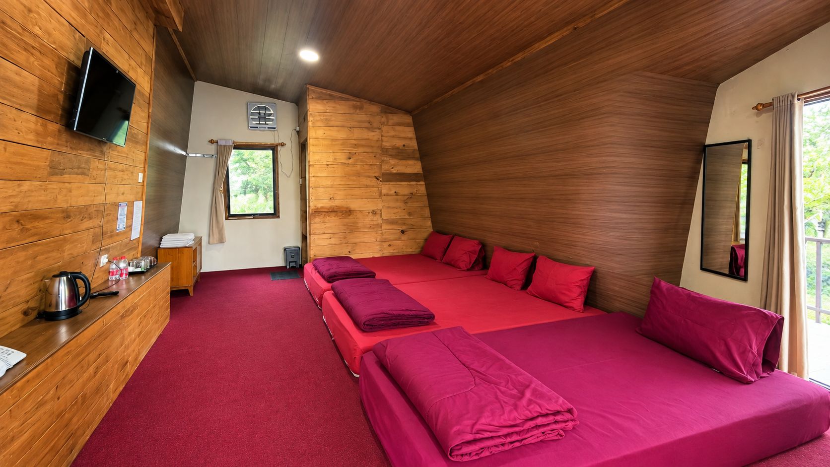 Habitación con paredes de madera, un televisor de pantalla plana montado en la pared, un escritorio con un hervidor y una ventana con cortinas.