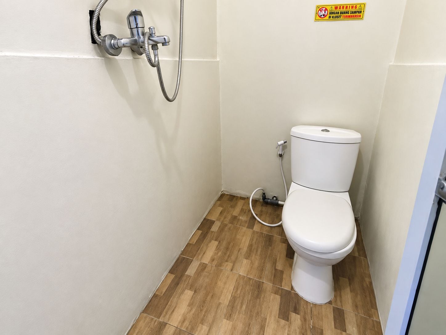 A small, clean bathroom with a toilet, a shower, and a visible warning sign.