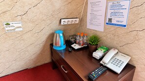 Een receptiebalie in een hotel, met een telefoon, koffiezetapparaat, flessen water, een plant en een bord met hotelregels.