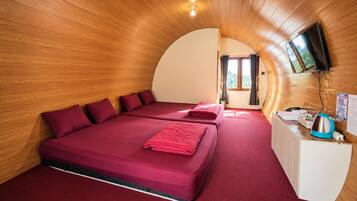A room with two beds, a wooden ceiling, a TV mounted on the wall, and a radiator.