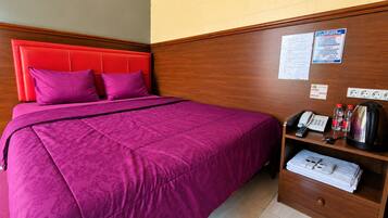 A hotel room with a bed, a wooden headboard, a bedside table with a phone, a kettle, and a folded towel.
