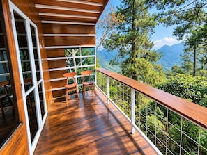A wooden deck with a railing, two chairs, and a view of mountains and trees.