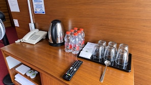 A hotel reception desk with a telephone, a kettle, bottled water, a tray with glasses and a spoon, and a remote control.