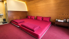 A double bed with red bedding, a wooden headboard, a bedside table with a phone, and a nightstand with toiletries.