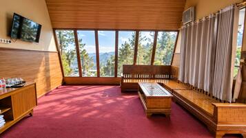 A room with a red carpet, wooden furniture, a television, and a large window with a view of trees and mountains.
