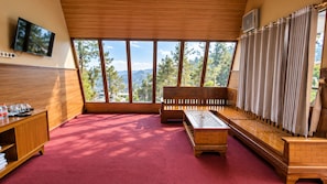 A room with a red carpet, wooden furniture, a television, and a large window with a view of trees and mountains.