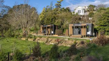 Ein modernes Haus mit einem großen Garten, zwei kleinen Holzhäuschen und einem Hauptgebäude mit Balkon.