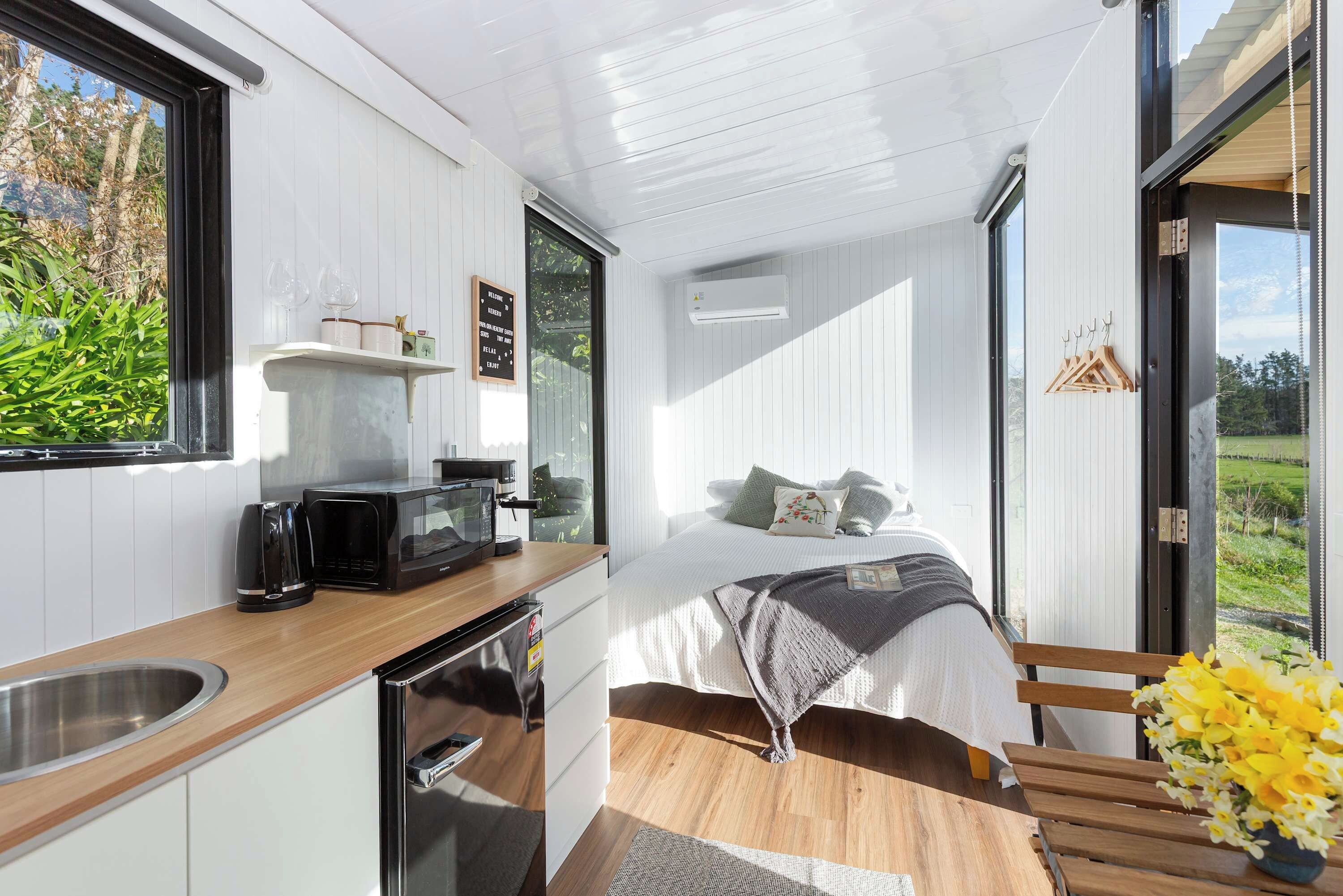 Ein gemütlicher Raum mit Bett, einer kleinen Küchenzeile und einem Fenster mit Blick auf Grünflächen.