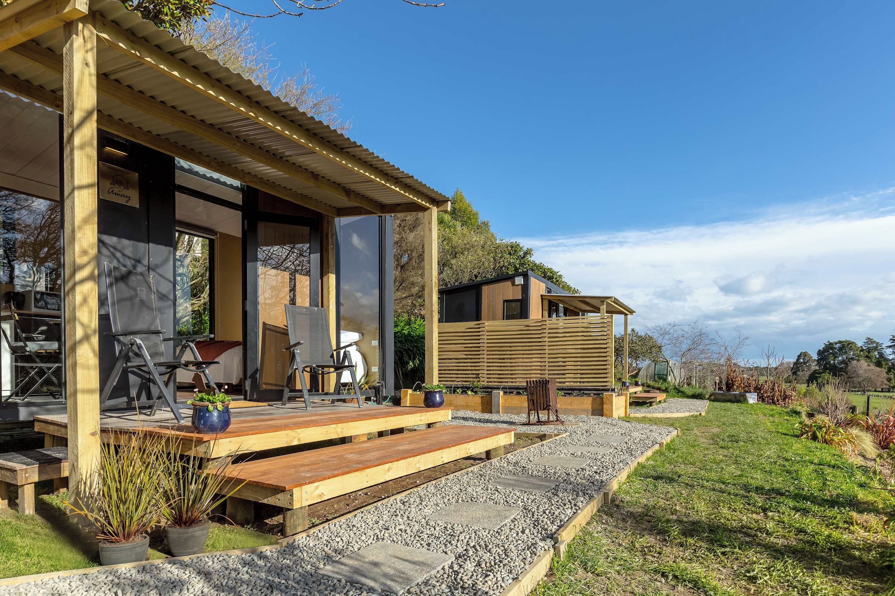 A modern outdoor seating area with wooden benches and chairs, a small stage, and a garden with gravel paths.