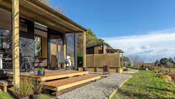 A modern outdoor seating area with wooden benches and chairs, a small stage, and a garden with gravel paths.