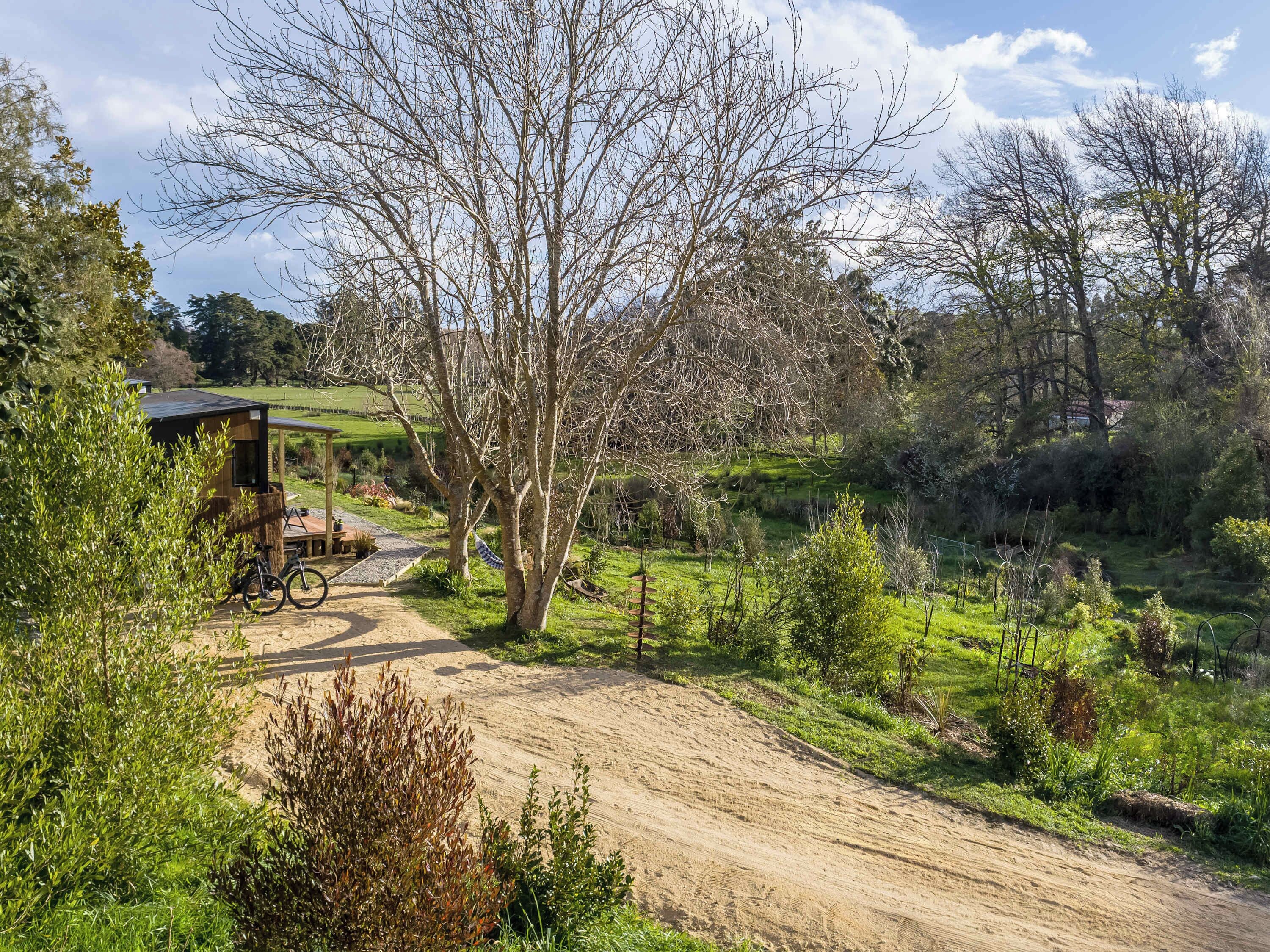A rustic cabin with a dirt path leading to it, surrounded by lush greenery and trees.