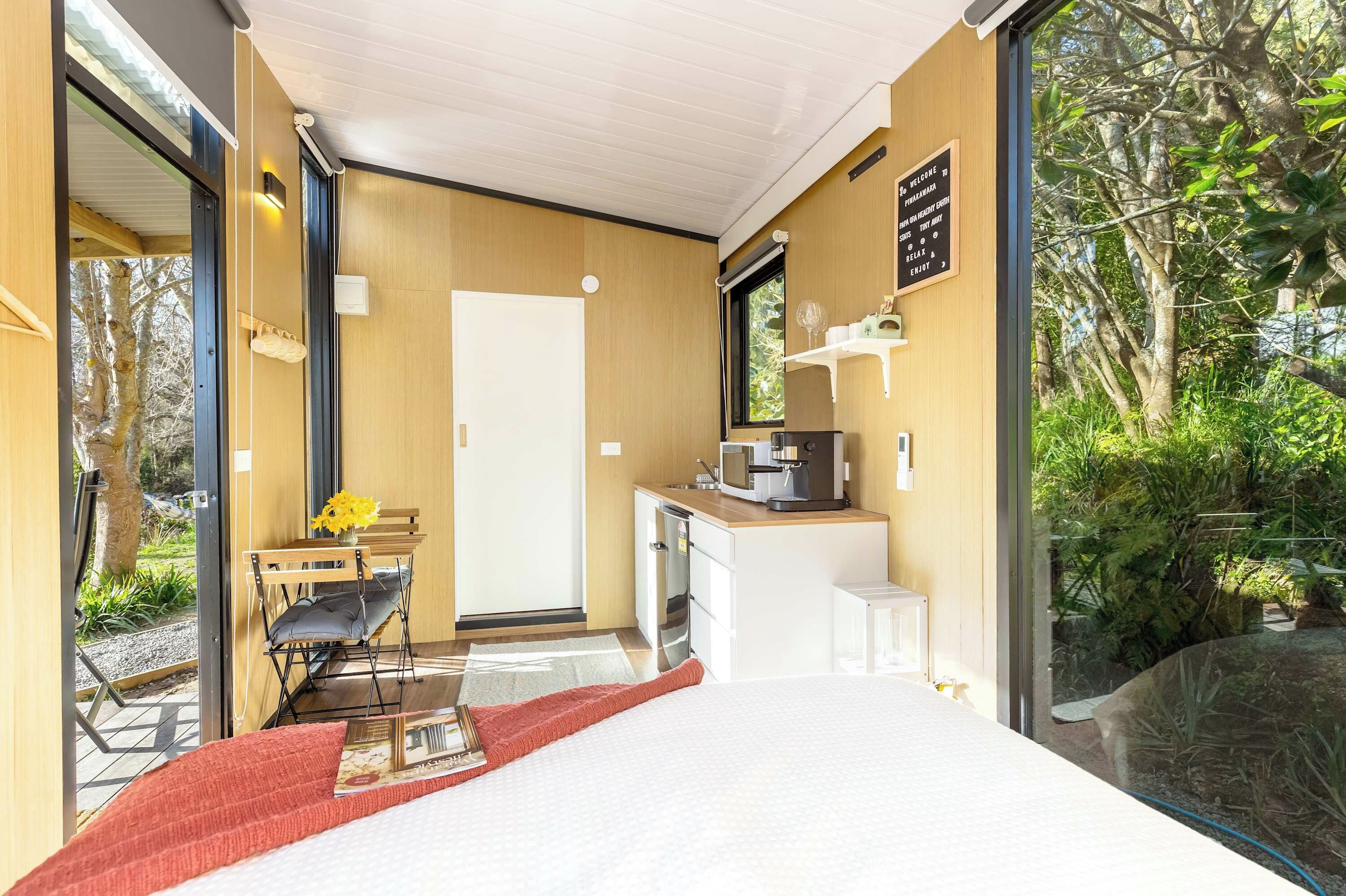 A modern, compact room with a bed, a small kitchenette, and a glass door leading to an outdoor area.