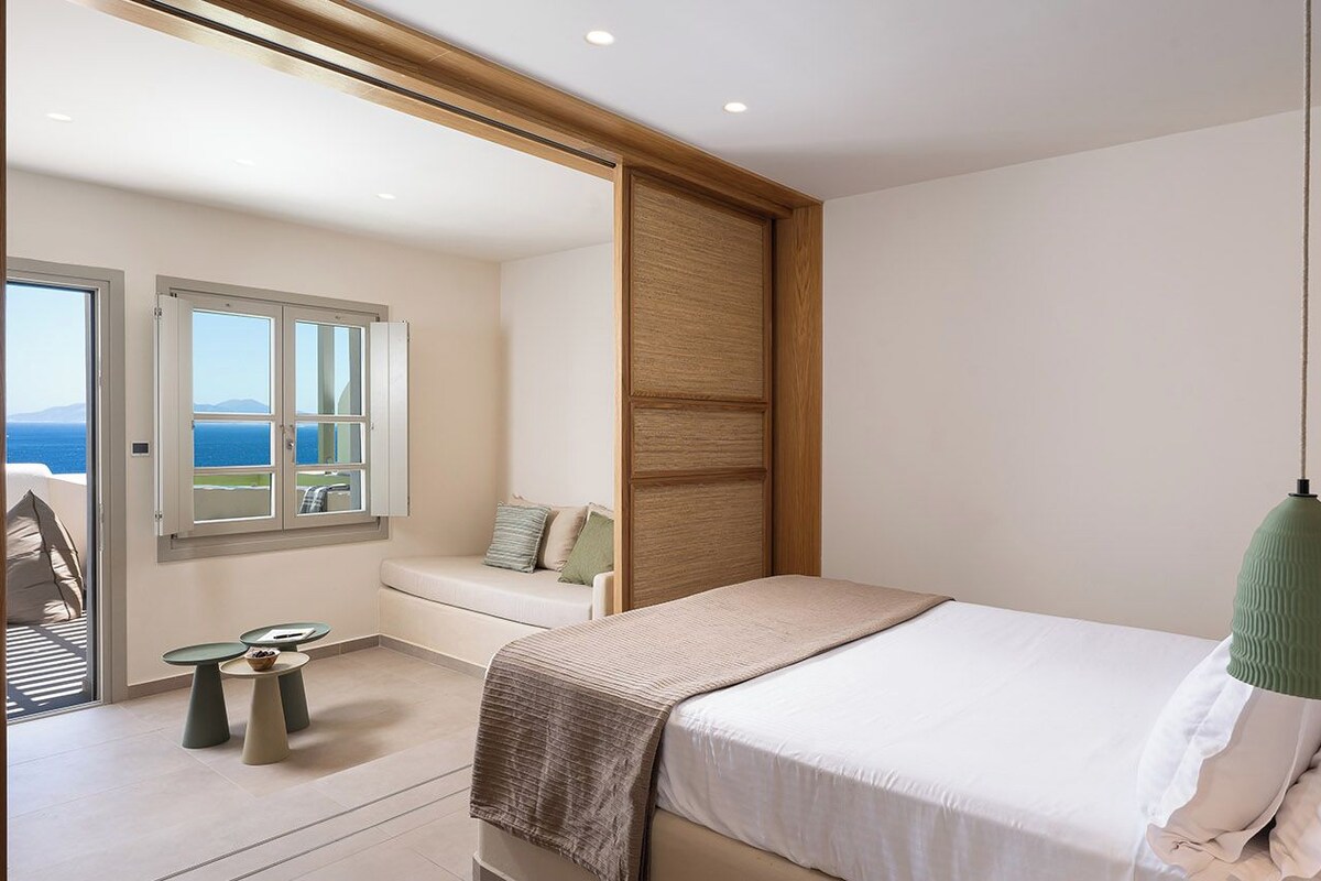 A bedroom with a bed, a seating area with a view, and a balcony.
