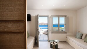 A room with a view of the sea, a sofa, a small table, and a door leading to an outdoor area. - Gea Perla Serifos (Serifos)