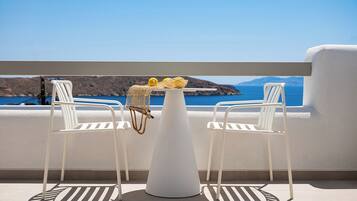 A white table with a basket containing lemons and a net, two white chairs, and a view of the sea and mountains.