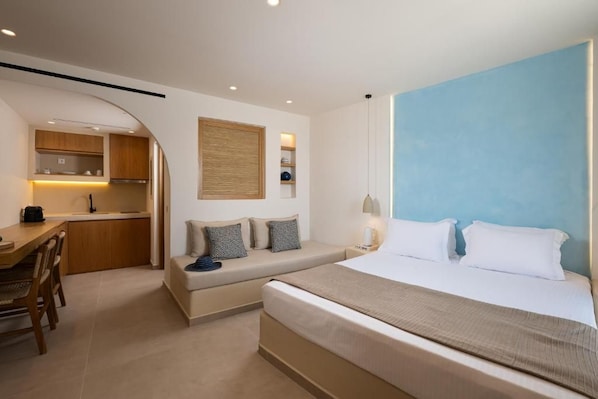 A compact hotel room with a bed, a small seating area, a kitchenette, and a view of the sky. - Gea Perla Serifos (Serifos)