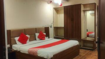 A bedroom with a large bed, wooden flooring, a wardrobe, and a ceiling fan.
