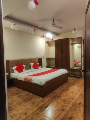 A bedroom with a large bed, wooden flooring, a wardrobe, and a ceiling fan.