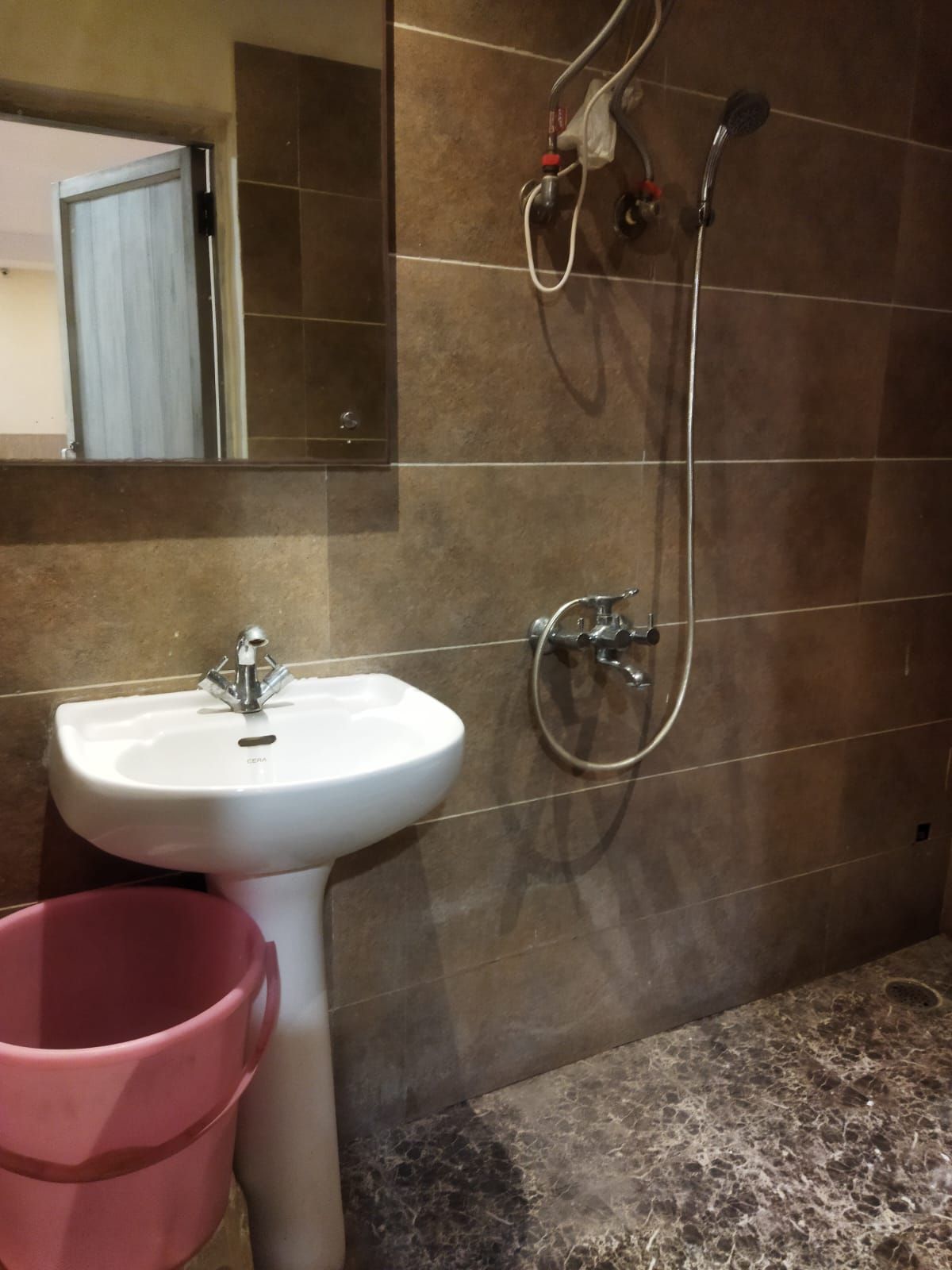 Un baño con un lavamanos blanco, un espejo y una ducha con cabezal de ducha de mano.
