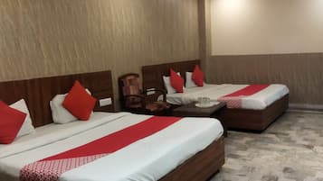 Habitación de hotel con dos camas, cada una con cabecero de madera, ropa de cama blanca y roja, y una mesita de noche con lámpara.