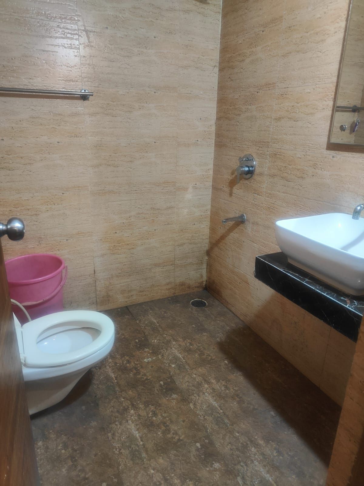 A small bathroom with a toilet, a sink, and a pink bucket.