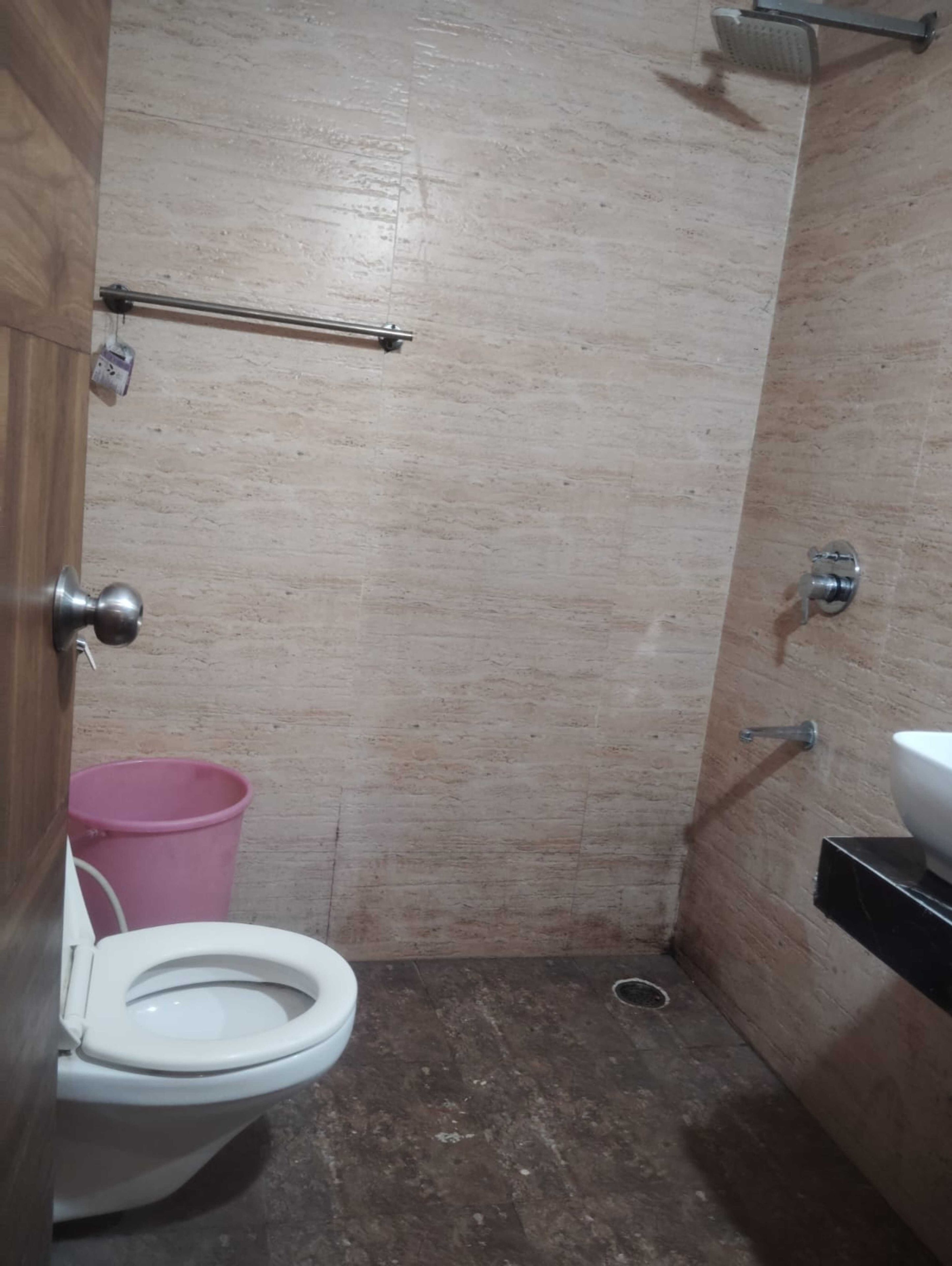 A small bathroom with a toilet, a pink bucket, a metal towel rack, and a sink.