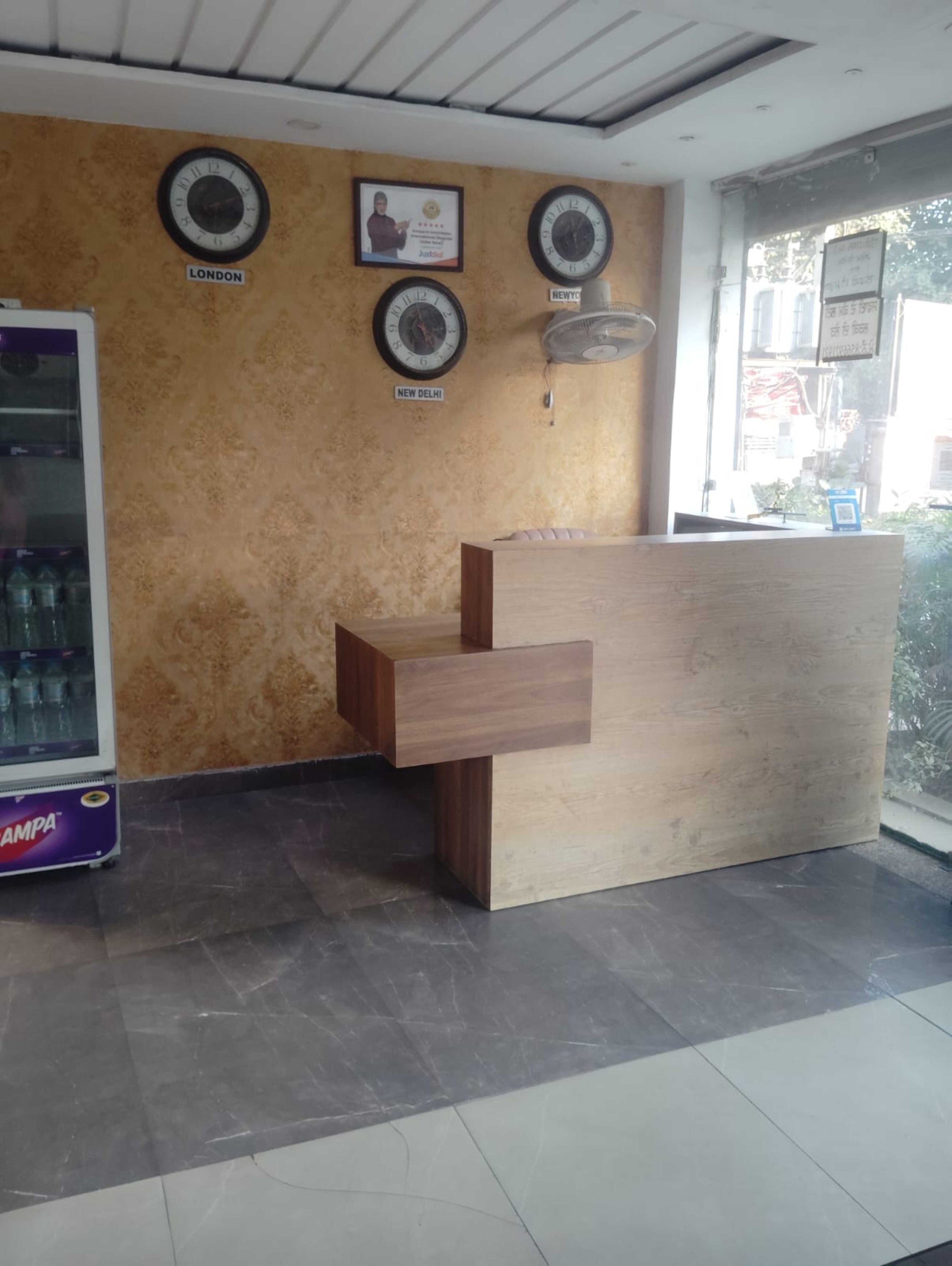 Un espace d’accueil avec un bureau en bois, des horloges murales et un réfrigérateur.