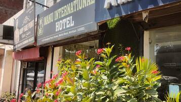 Exterior del Hotel Manu International con un cartel visible, un mostrador de información turística y un muro de ladrillo.