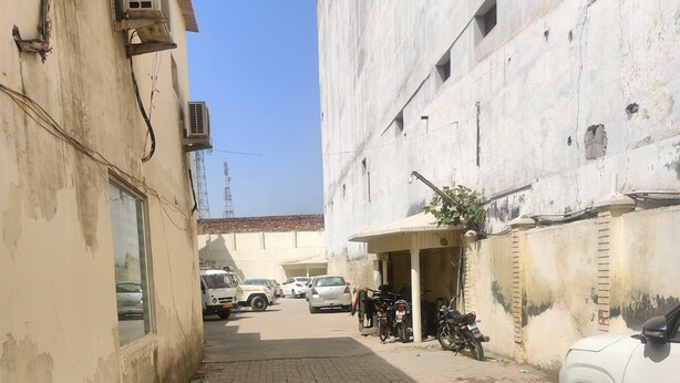 A narrow paved alleyway with a white car parked on the right and several motorcycles on the left. - Hotel Amaze Inn (Amritsar)