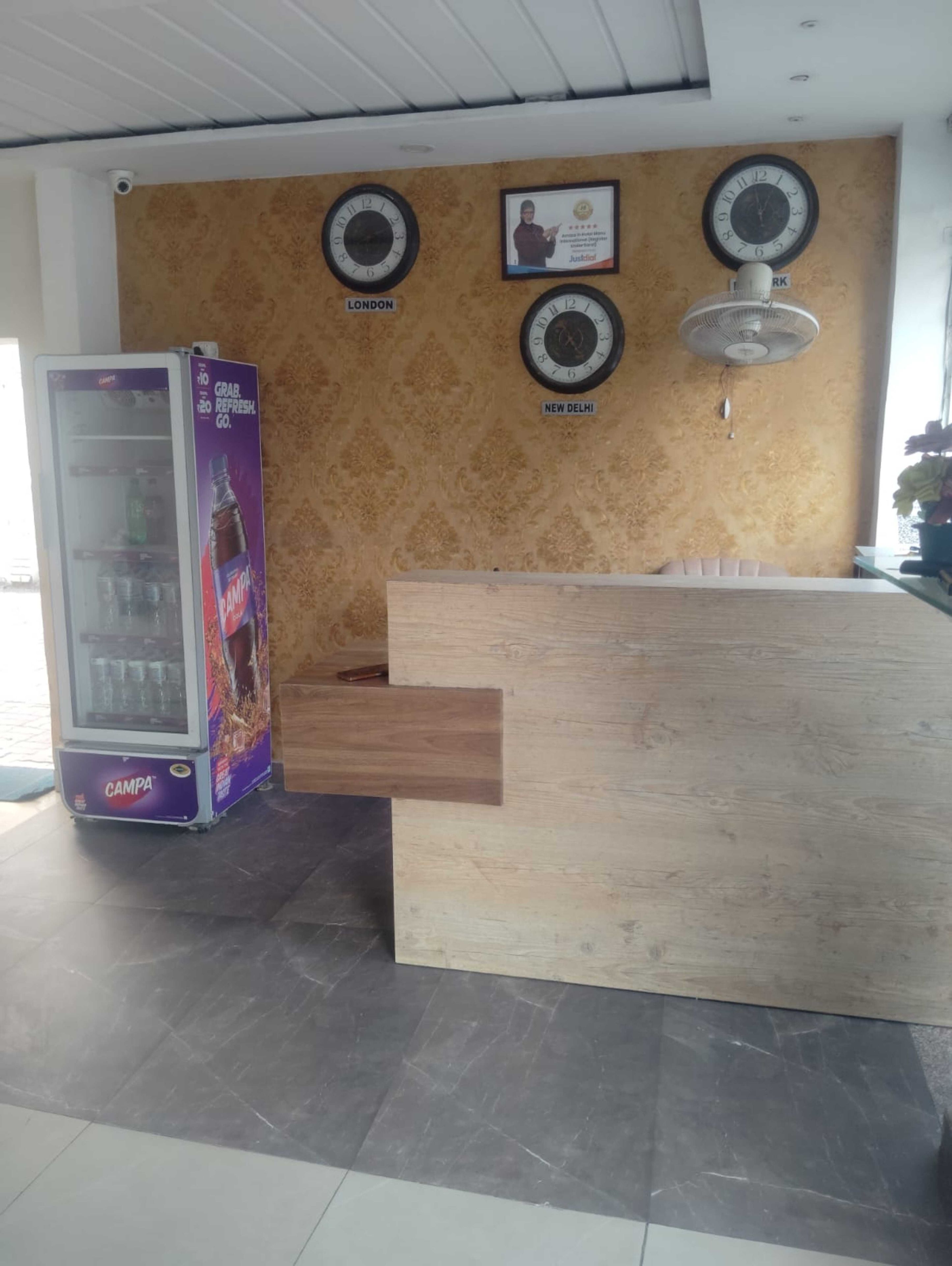 Un comptoir d’accueil avec une horloge, un certificat encadré et une horloge murale indiquant l’heure de Londres et de New Delhi.