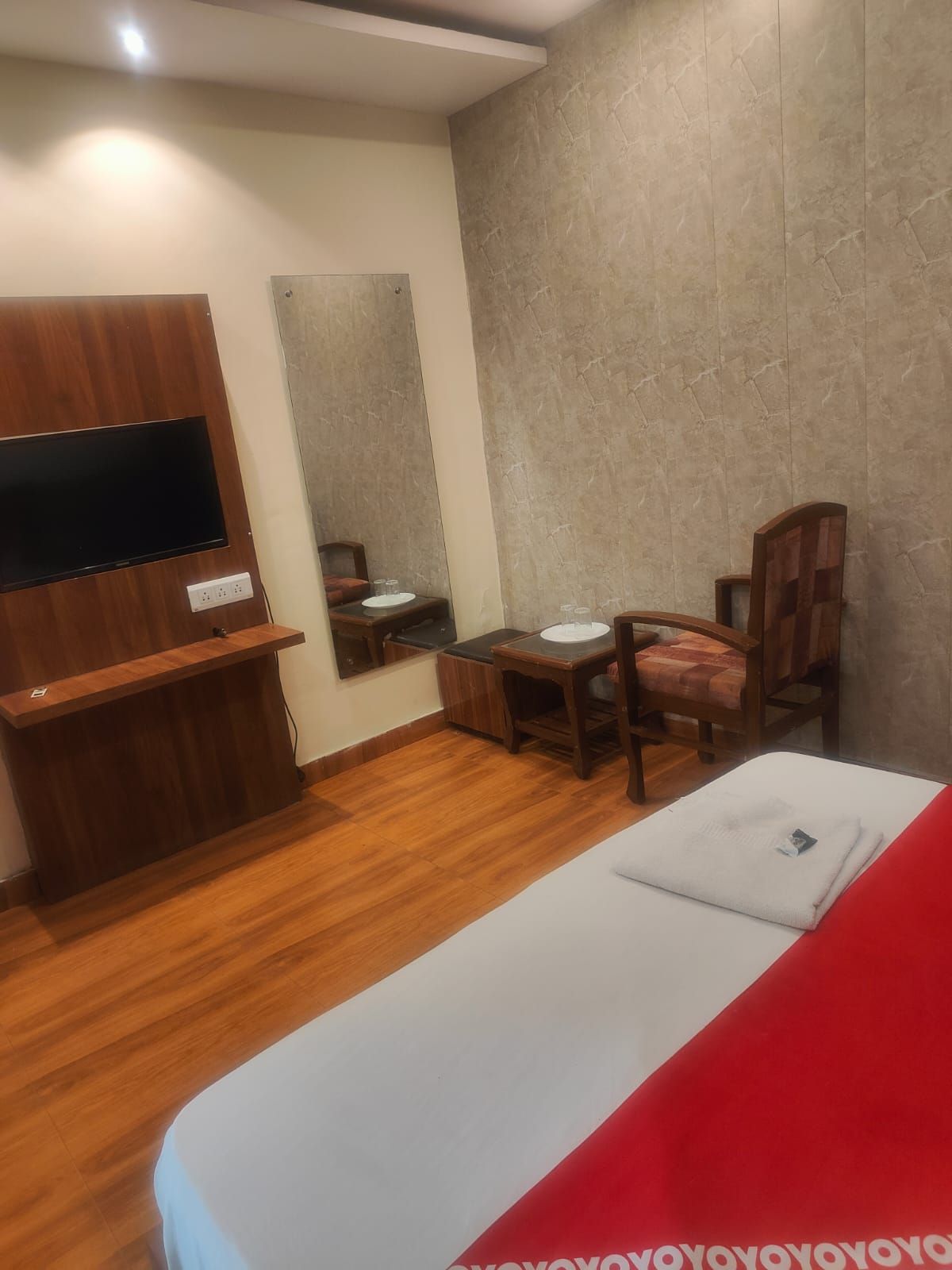 A hotel room with a bed, a desk, a chair, a television mounted on the wall, and a mirror.