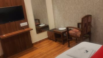 A hotel room with a bed, a desk, a chair, a television mounted on the wall, and a mirror.