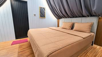 A bedroom with a bed, a headboard, a window with curtains, and a wooden floor.
