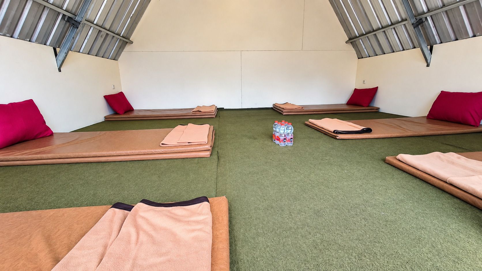 A room with four mats arranged in a square, green carpeted floor, and a small water bottle in the center.