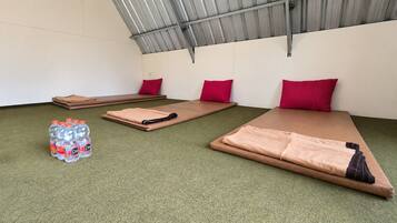 A room with three mats, each with a red pillow, and a stack of bottled water on the floor.