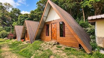 A series of wooden cabins with pitched roofs, set in a lush, green environment.