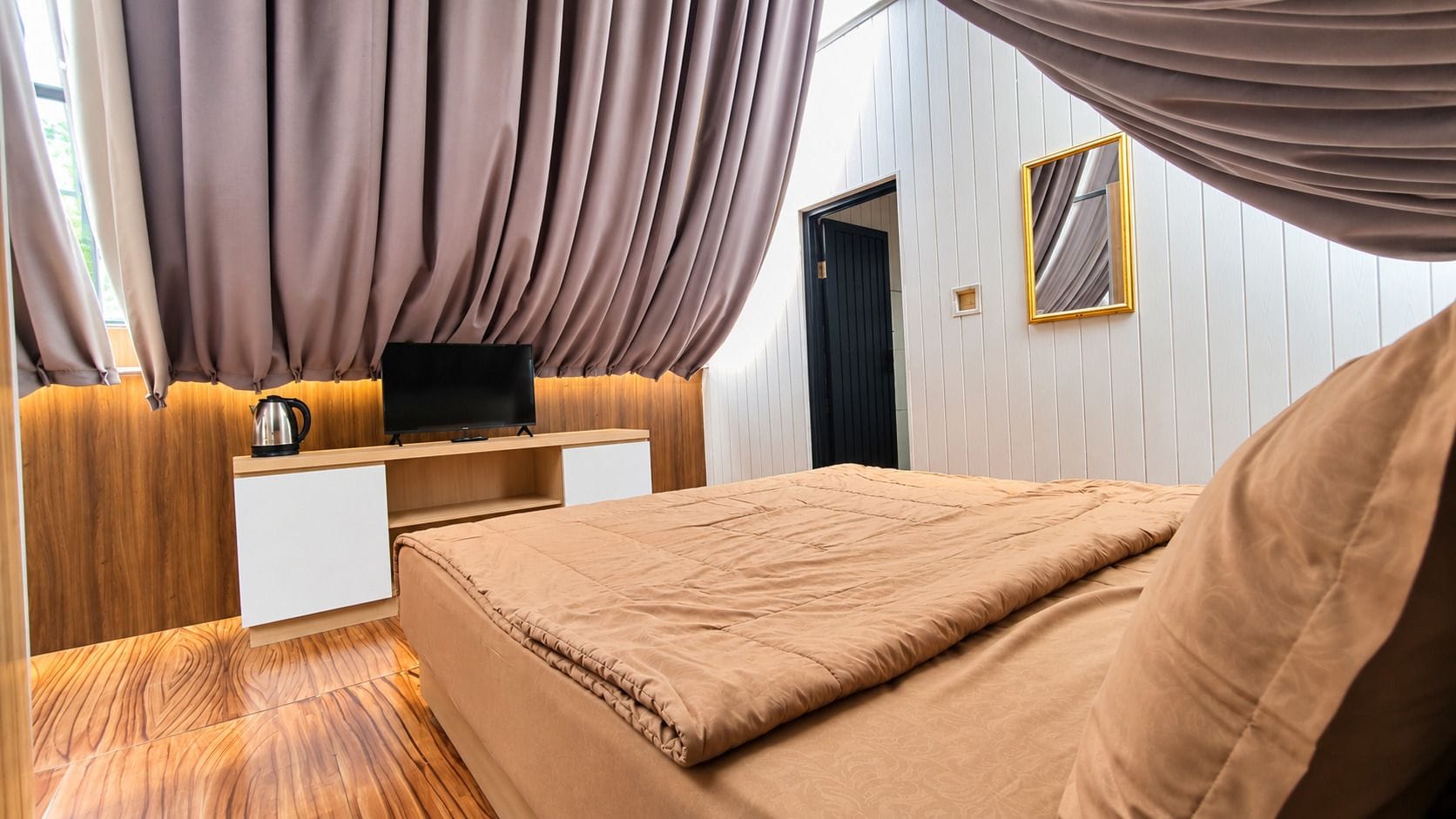Un dormitorio con cama, escritorio, televisión y ventana con cortinas.