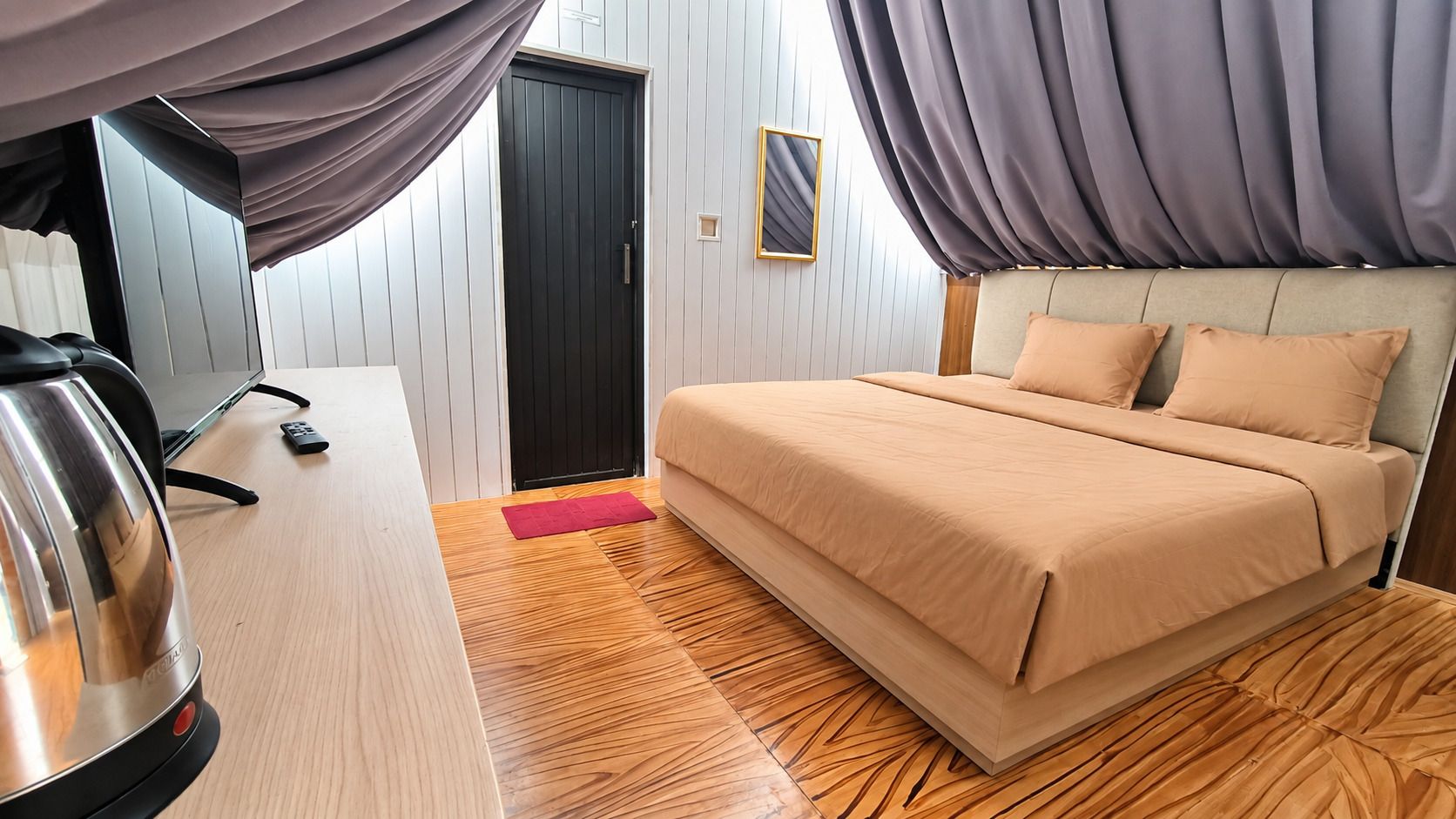 A hotel room with a bed, a desk, a kettle, and a door.