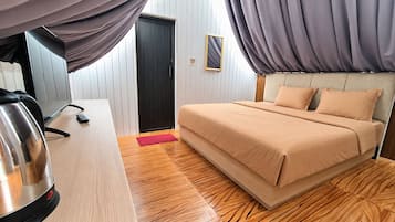 A hotel room with a bed, a desk, a kettle, and a door.