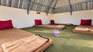 Una habitación con cuatro camas, cada una con una almohada roja y una manta marrón. Hay una pila de mantas dobladas y un montón de botellas de agua en el suelo.