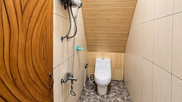 Une petite salle de bain aux murs lambrissés, avec des toilettes blanches, une pomme de douche et un radiateur fixé au mur.